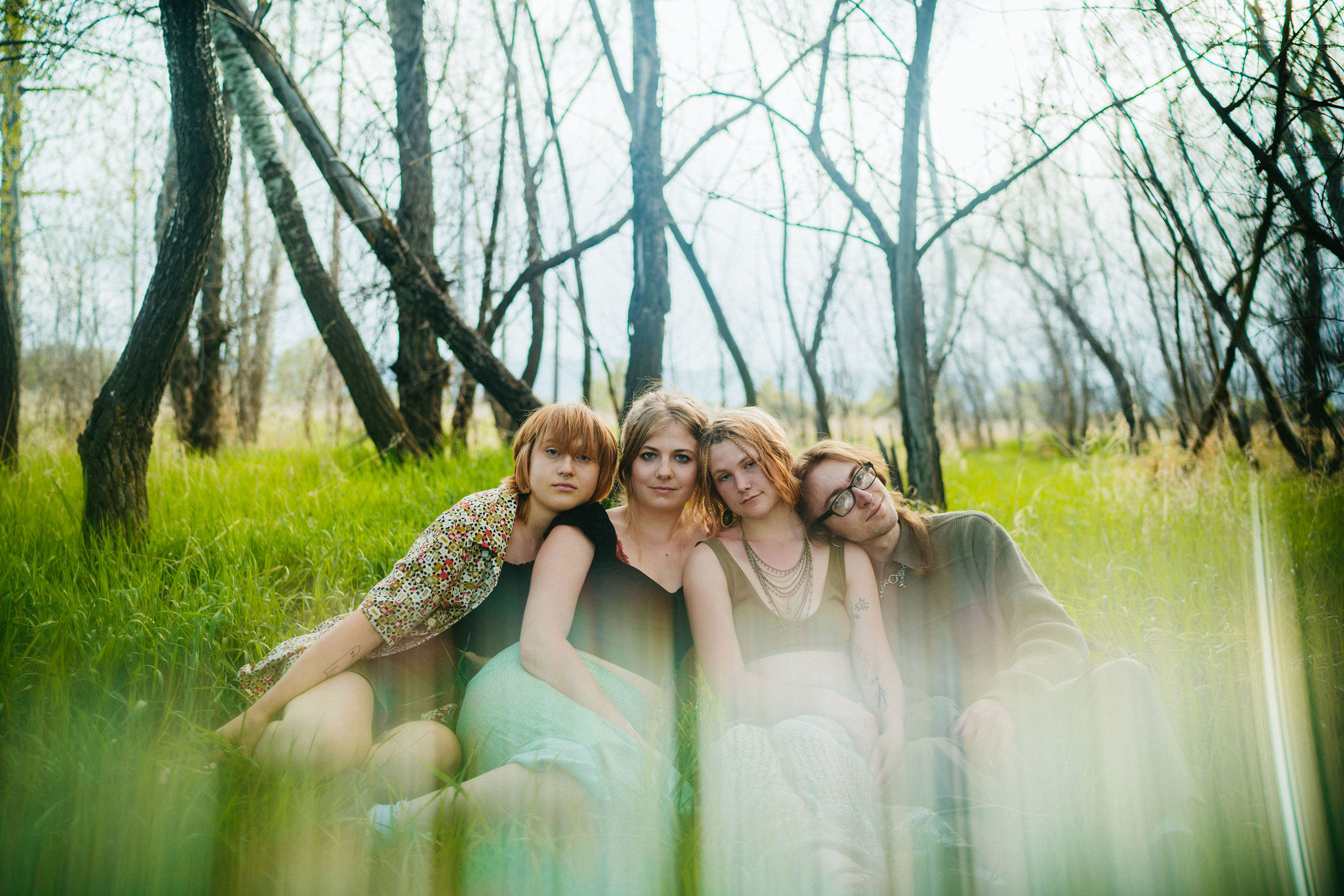 Four women sitting in grass surrounded by trees.