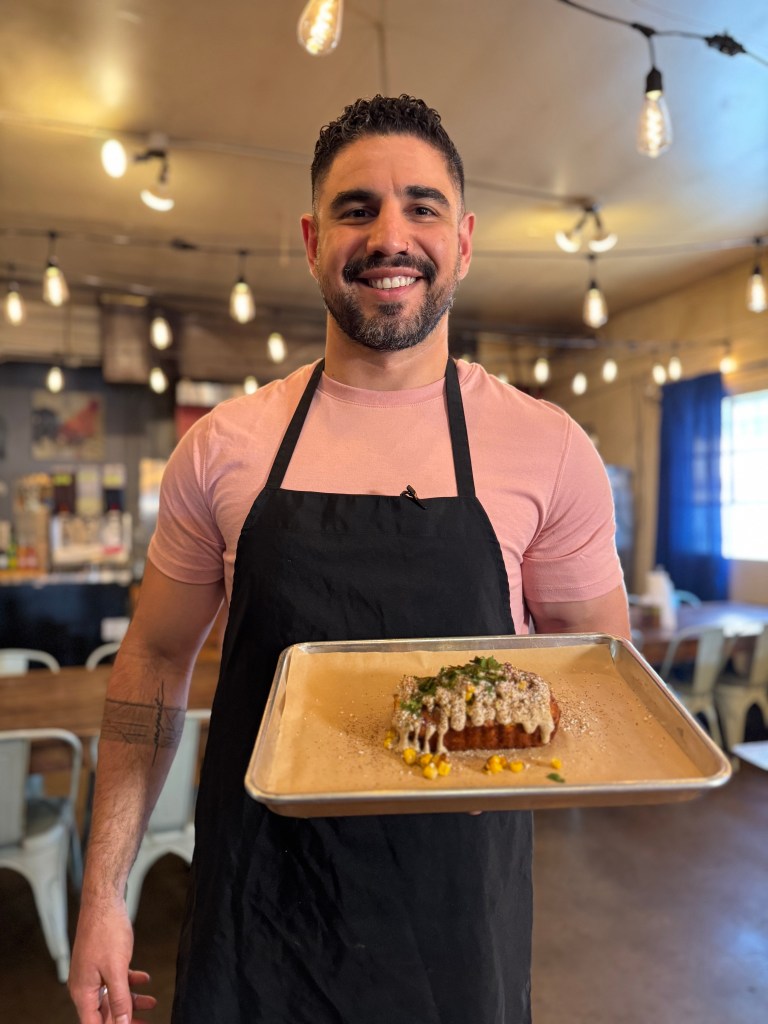 Manny Barella holding a tray of esquites cornbread from Riot BBQ