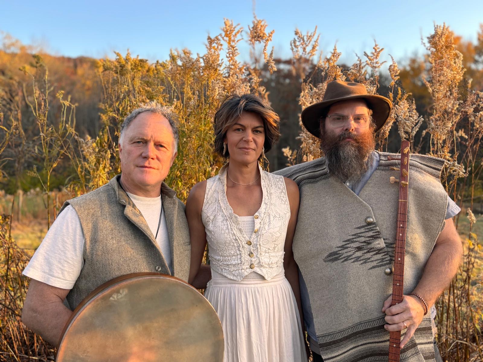 a man, woman and man hold instruments in front of a field