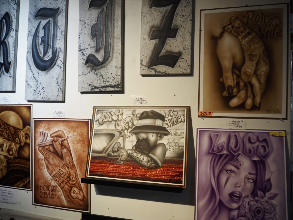 Art hangs on a wall, a few of them marked with "sold" stickers.