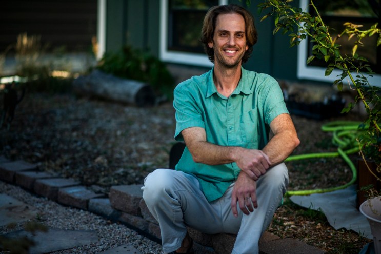 man in green shirt outside by plant