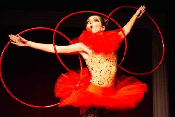 A clown wearing a red tutu juggles Hulu hoops.