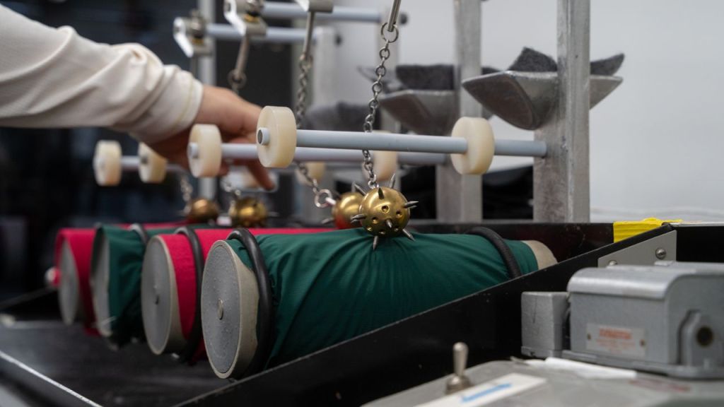 Spiked metal balls bouncing against fabric stretched across rotating cylinders