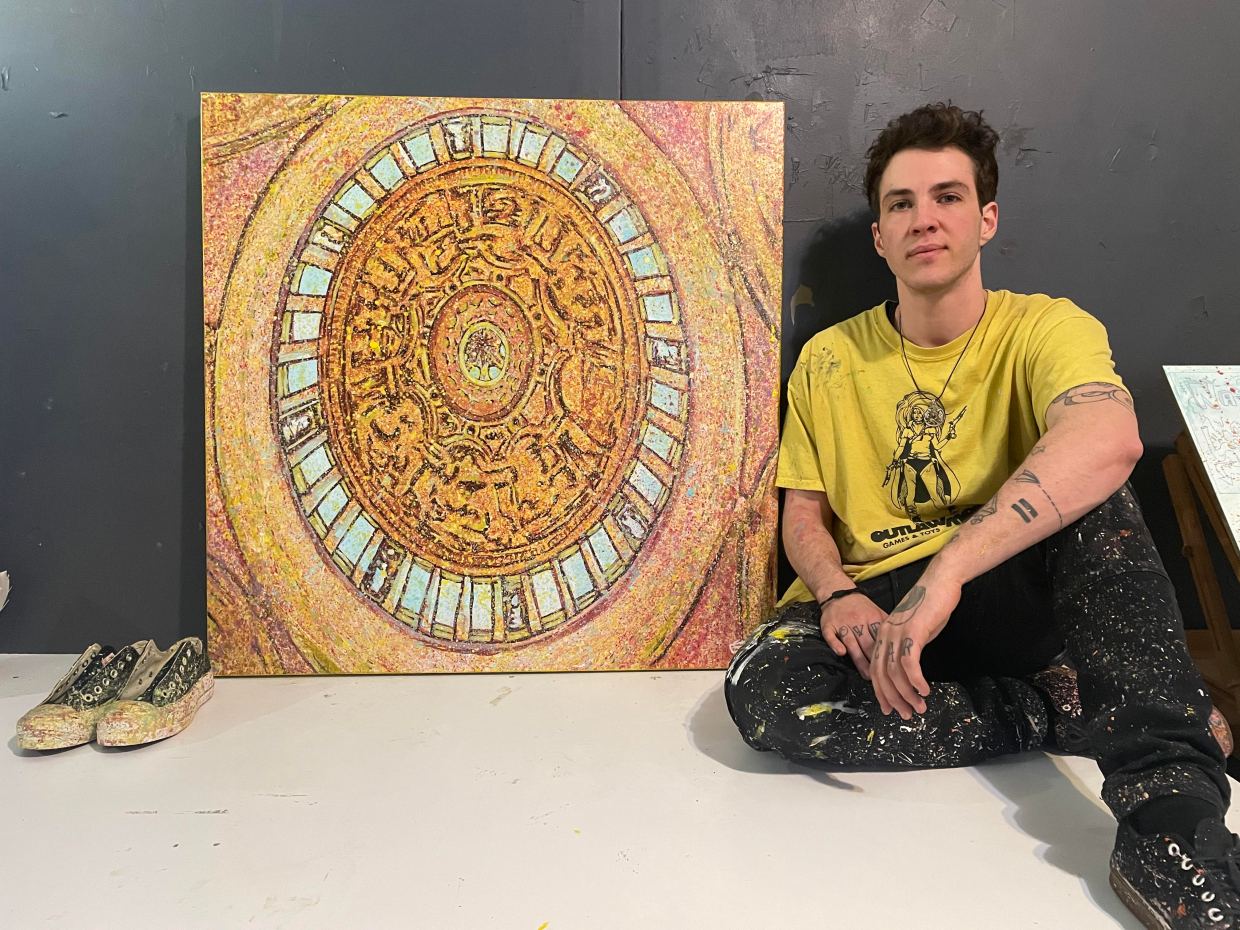 An artist sits by their painting.