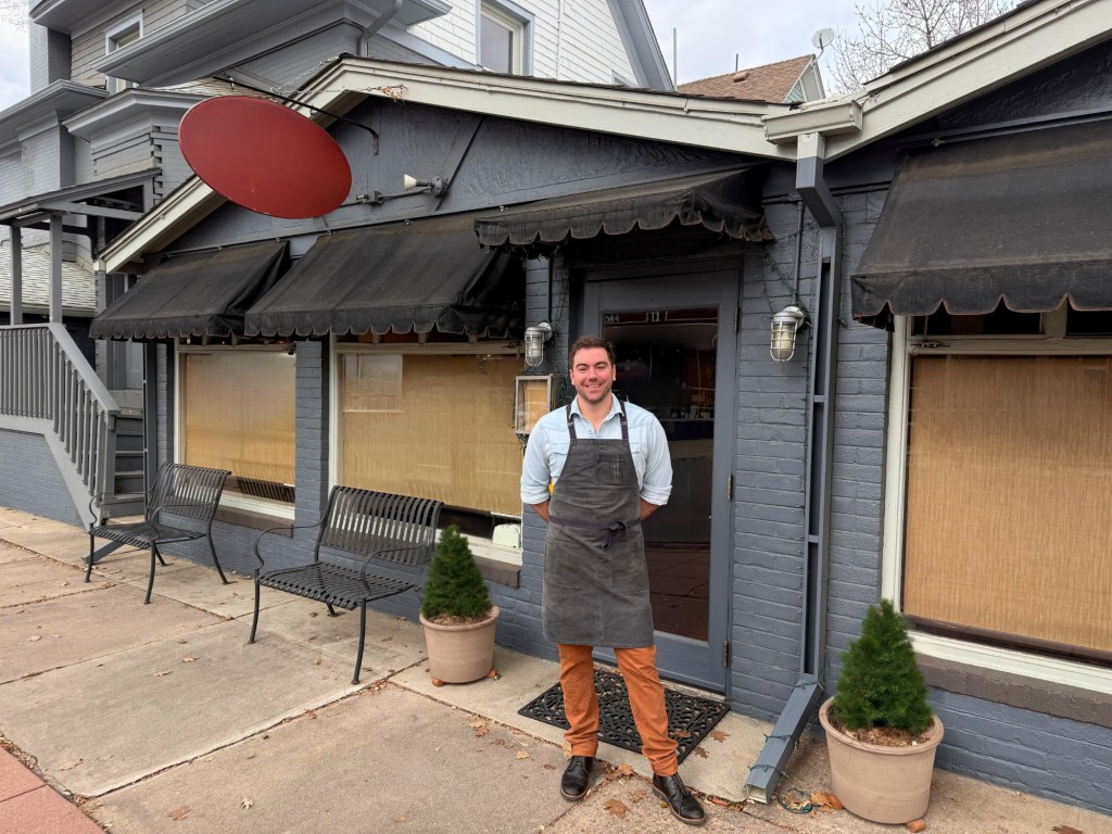 man in apron standing in front of a building