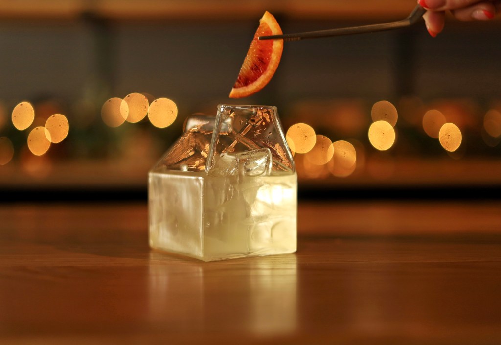 An orange garnish being placed on the non-alcoholic milk punch from Olivia, which is served in a milk box-shaped glass