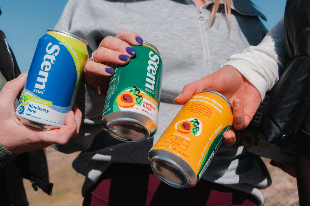 A close-up of three people holding cans of Stem Zero flavors