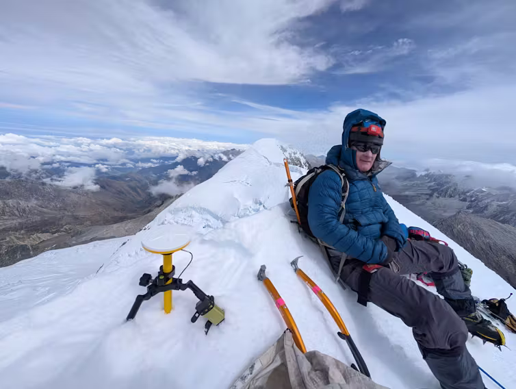 man sits on snow mound at mountain summit