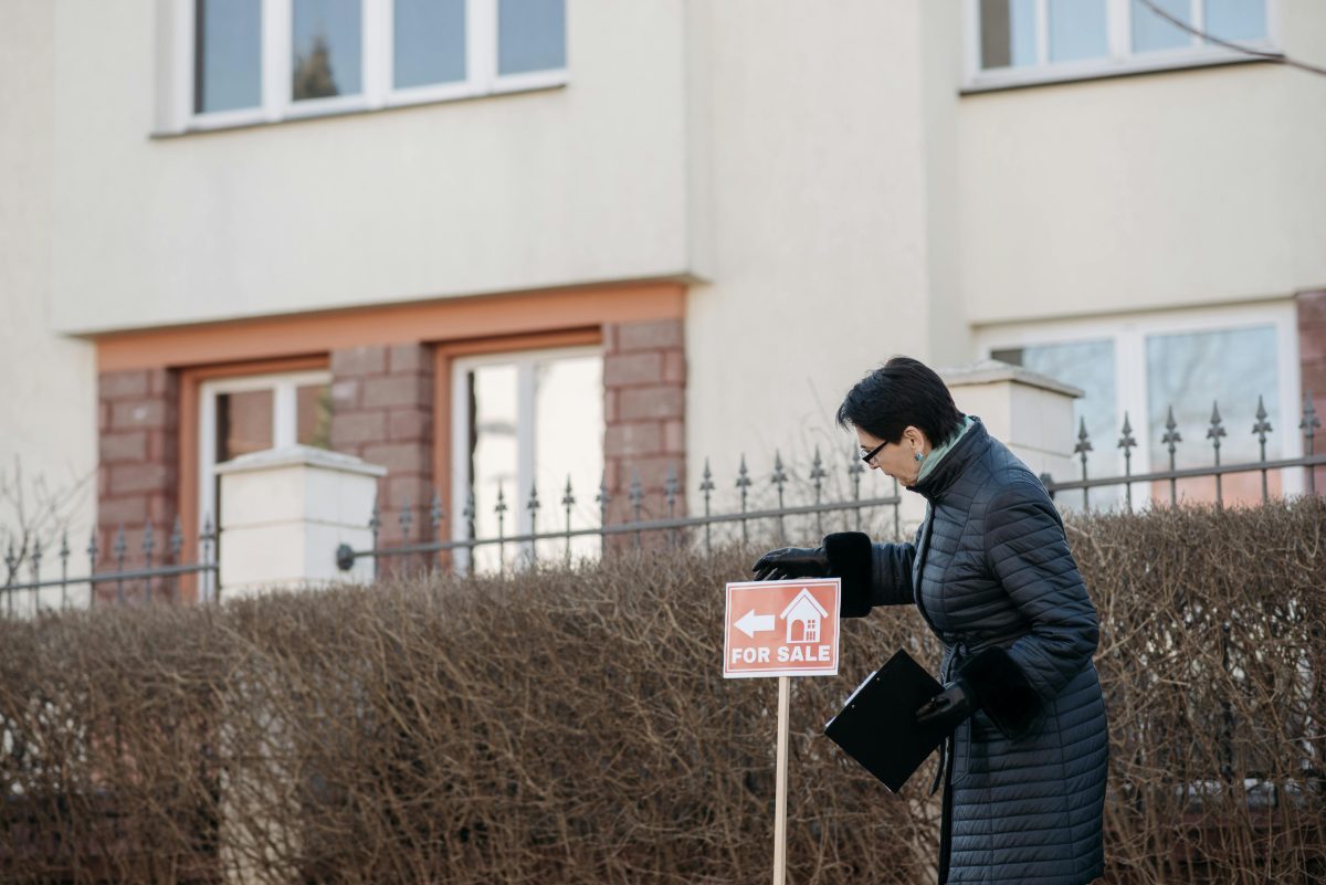 A woman standing next to a home for sale sign.