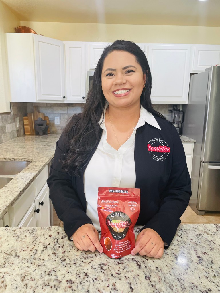 Camacho in a black Bombitas-branded jacket, posed with a birria bomb package