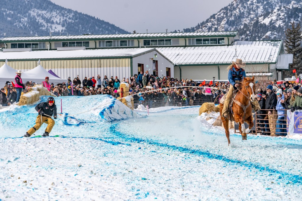Crowds in Estes Park surrounding a person on horseback with a skier in tow