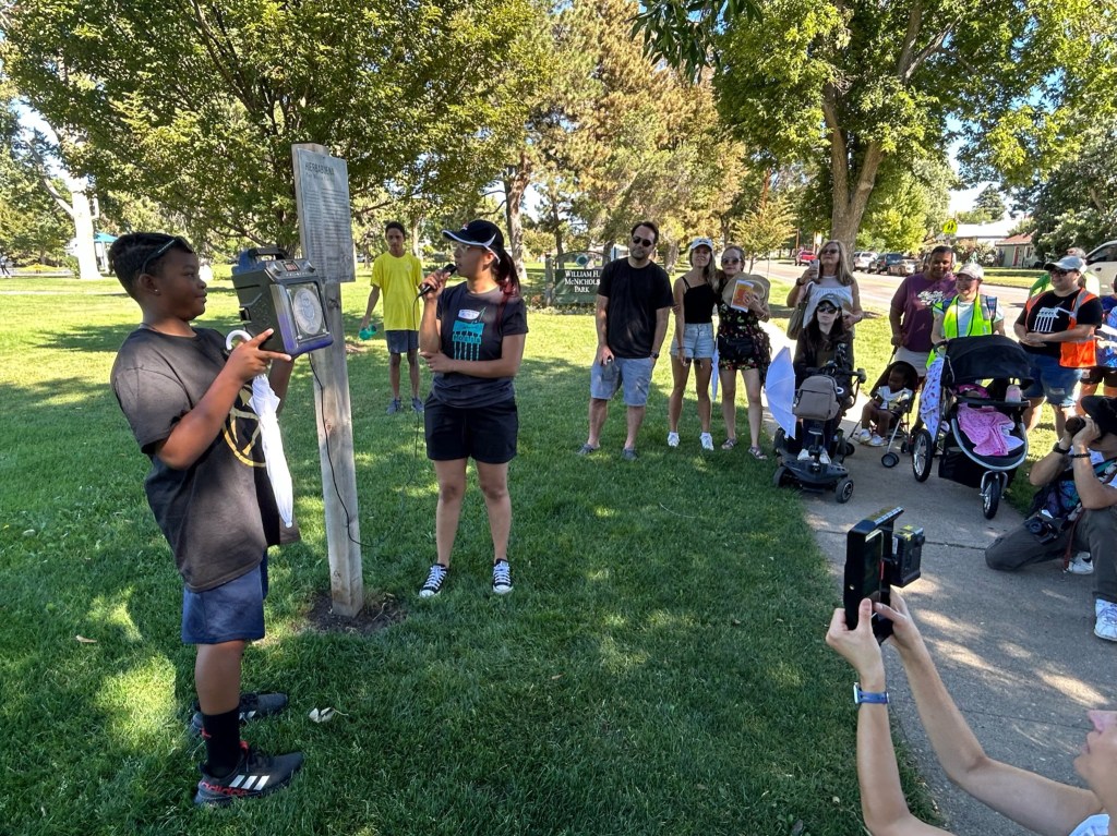 People gather around a sign in a park