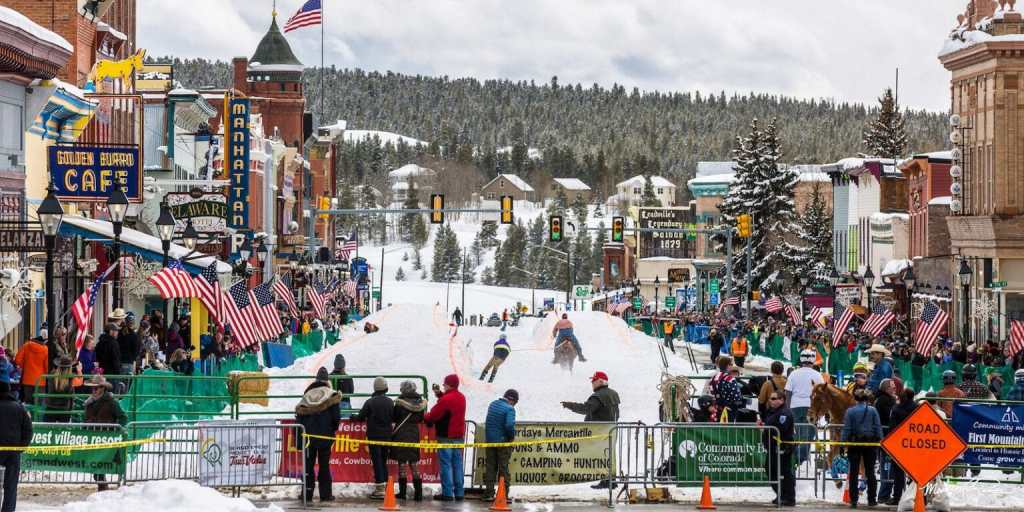 A skijoring team amid Victorian buildings and American flags in downtown Leadville