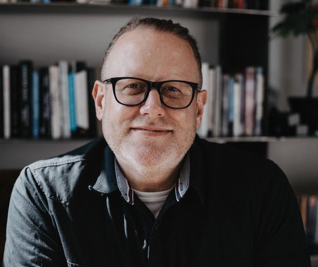 A portrait of a man in front of a book shelf