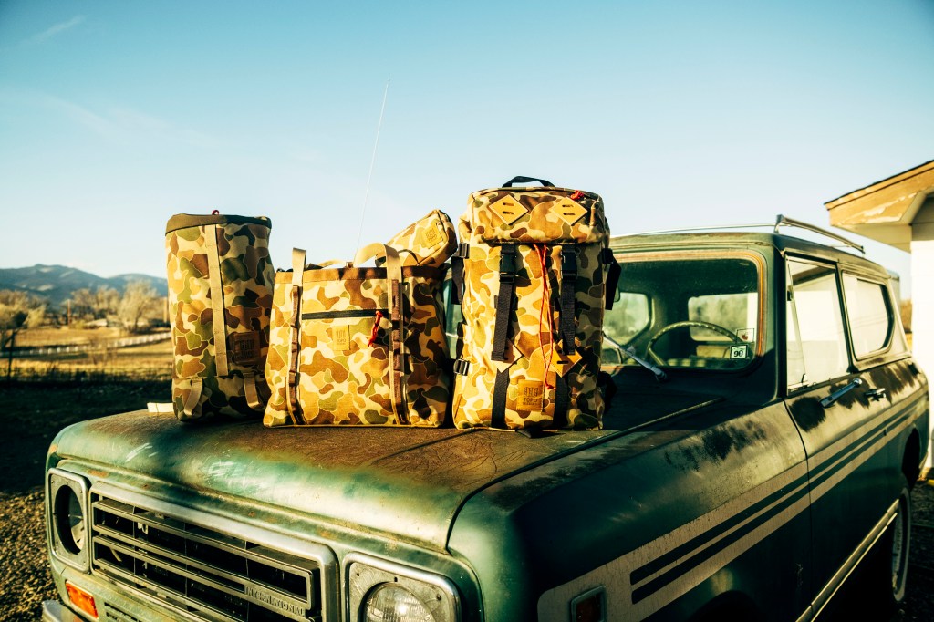 Camo-printed bags and packs from Topo Designs resting on the hood of a vintage vehicle