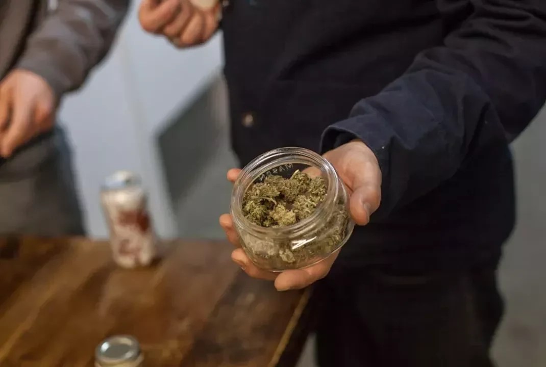 Man holds open jar of weed
