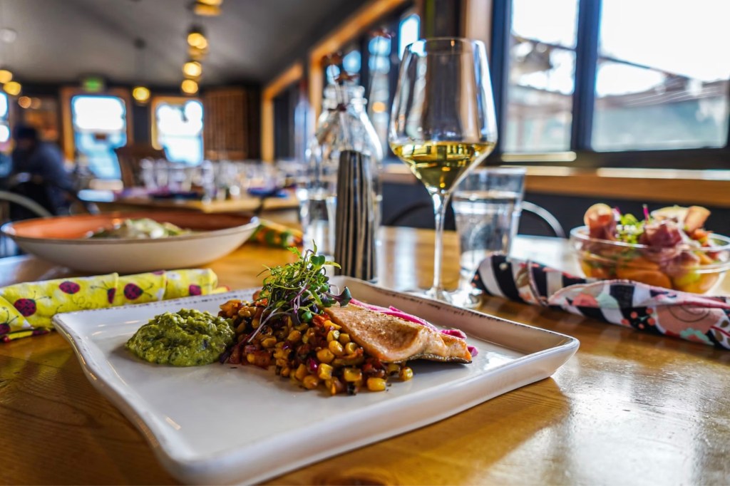 A fish entree, a glass of white wine and other menu items from Bird & Jim