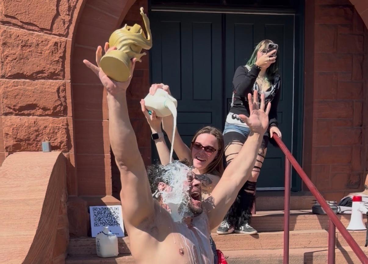 the winner of the Denver Milk off drinking challenge celebrates with his trophy while milk is poured over his head