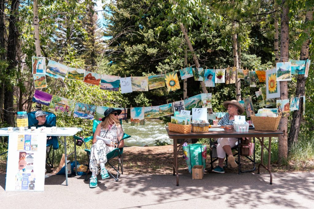 Watercolor paintings hung between trees on the Silverthorne riverwalk during a Sunday Art Stroll