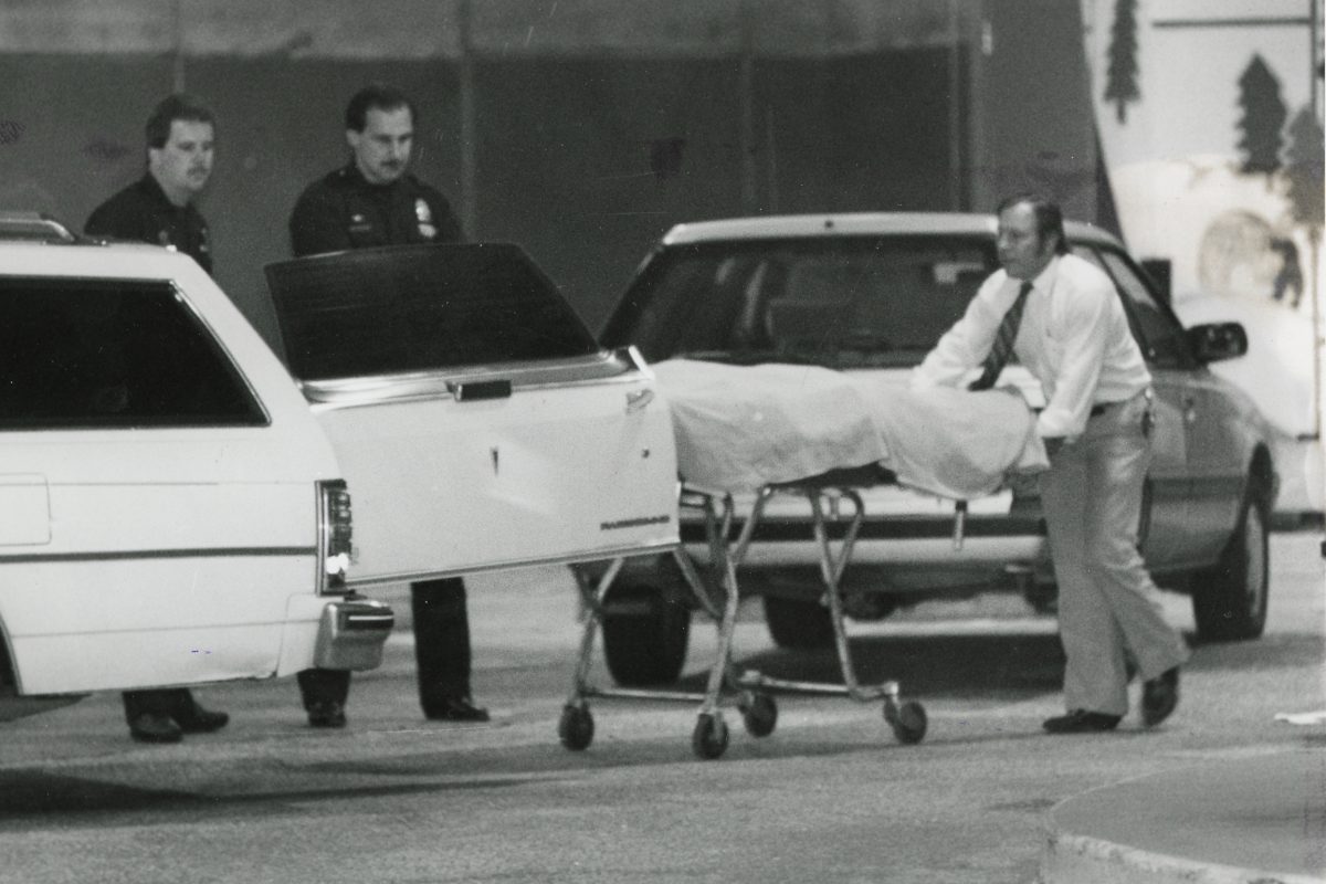 Law enforcement officials wheel out a covered dead body in the aftermath of the Father's Day bank massacre.