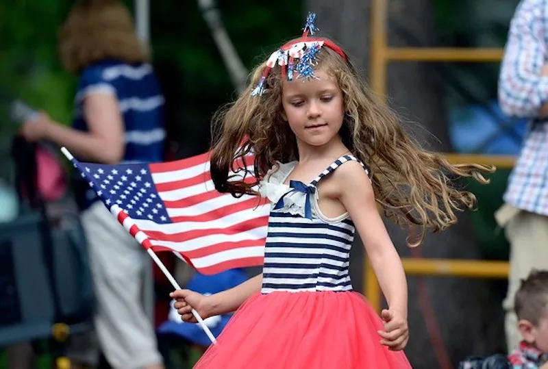 A young girl in red, white and blue holding an American flag
