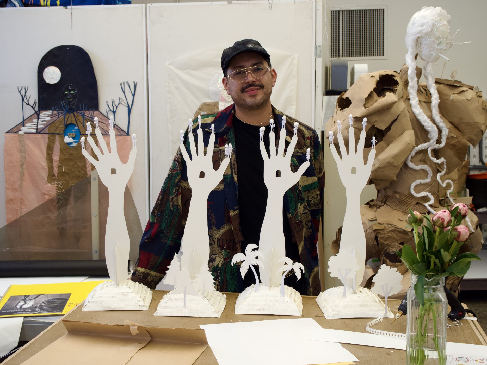 An artist stands next to paper hands