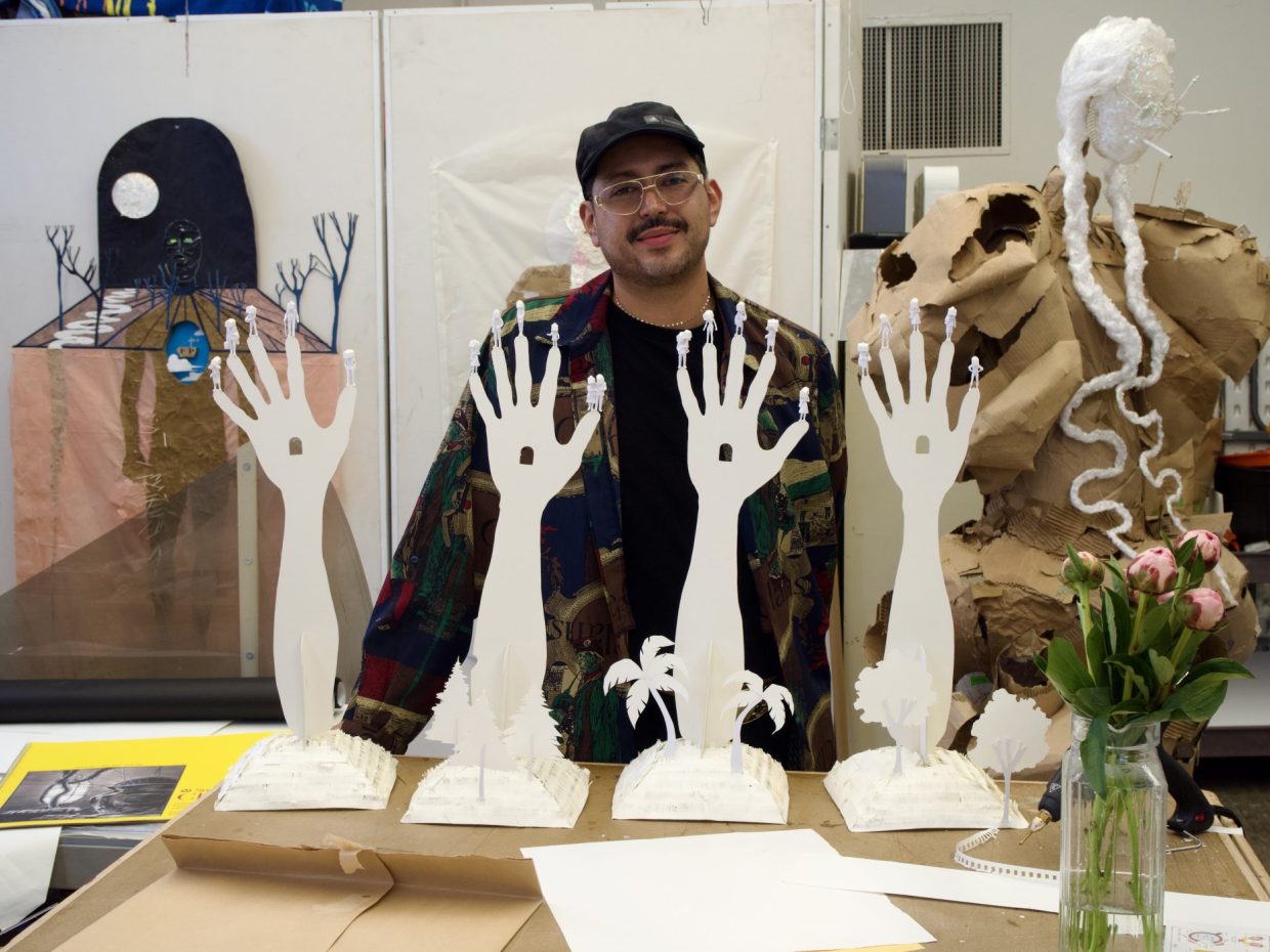 An artist stands next to paper hands