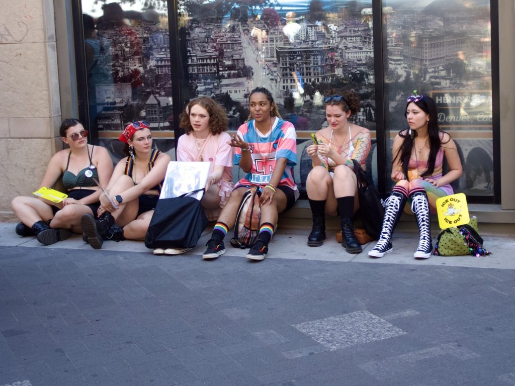 A group of friends sits on the ground at PrideFest