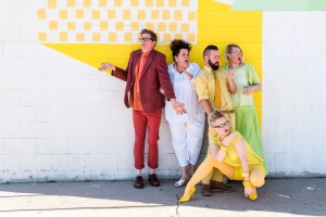 five people in colorful clothes stand next to a yellow and white wall