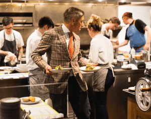 a man in a suit holding plates in a kitchen