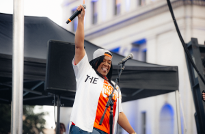 woman holds up a microphone on stage and smiles