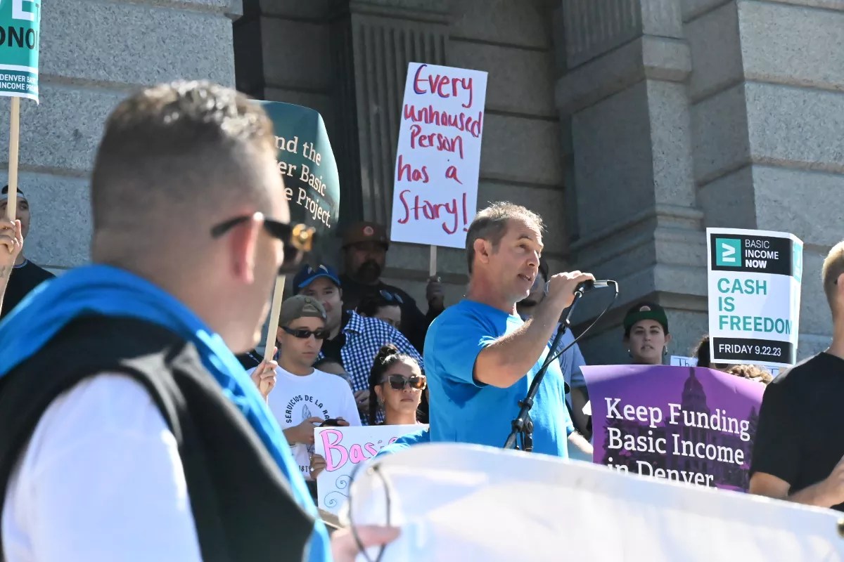 A man listens to another speak to a crowd.