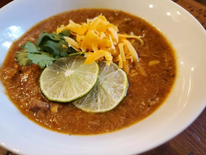 a bowl of green chile with limes, cheese and cilantro on top