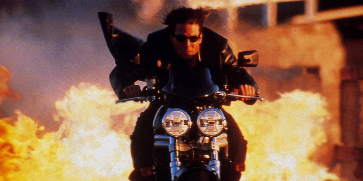 Tom cruise on motorcycle with fire behind him
