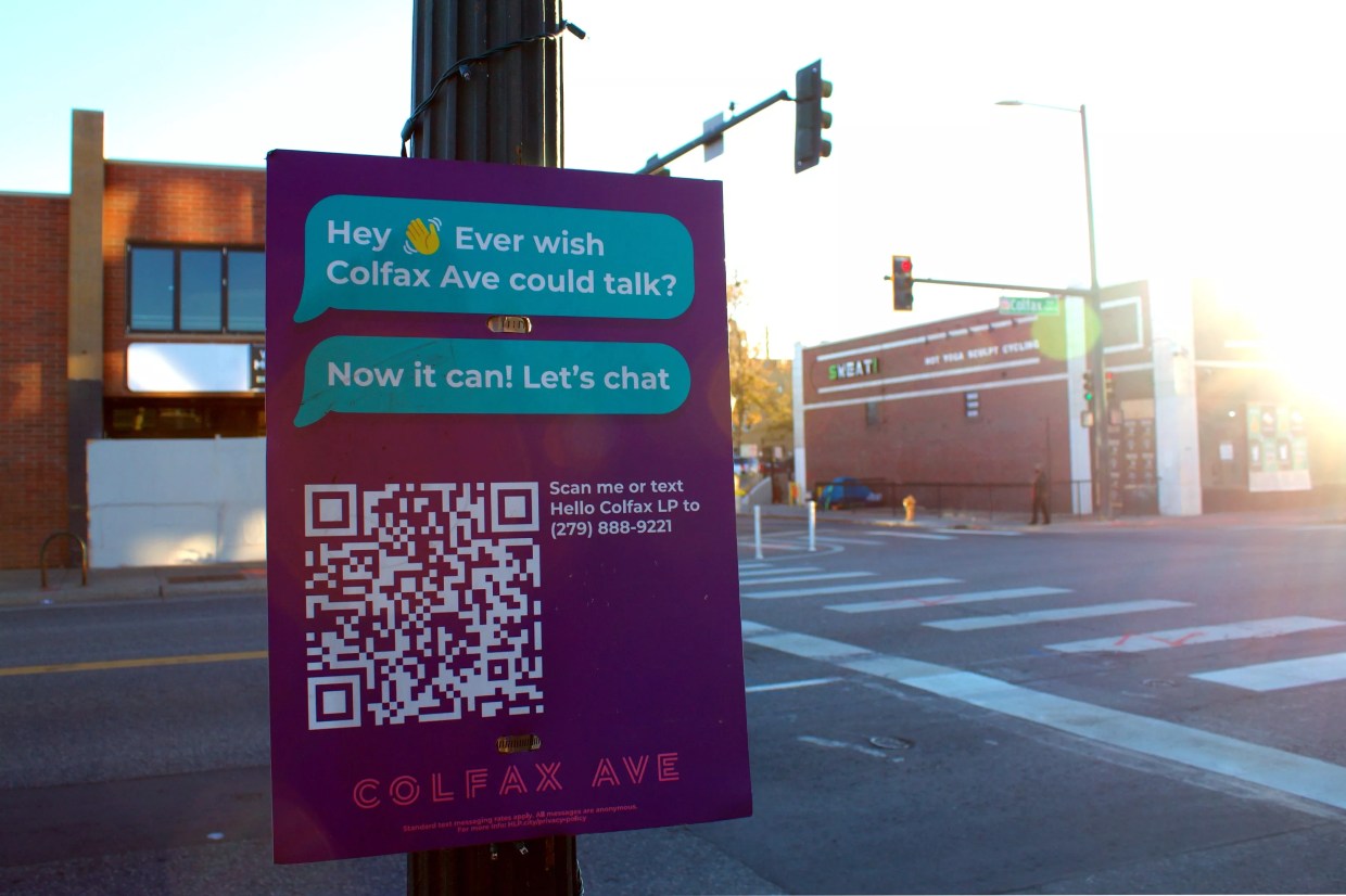 A sign posted on Colfax Avenue with a QR code, asking people to scan it to talk to Colfax.