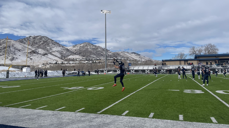 An athlete wearing dark blue and number 14 catches a football.