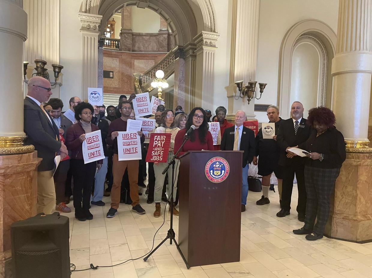 A group of rideshare drivers and advocates stand behind a podium