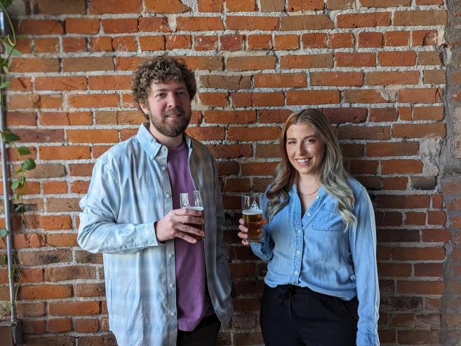 A man and a woman stand in front of a brick wall.