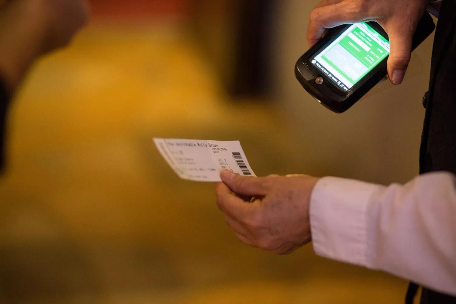 A ticket is held in one hand and scanned with the other by an attendee.