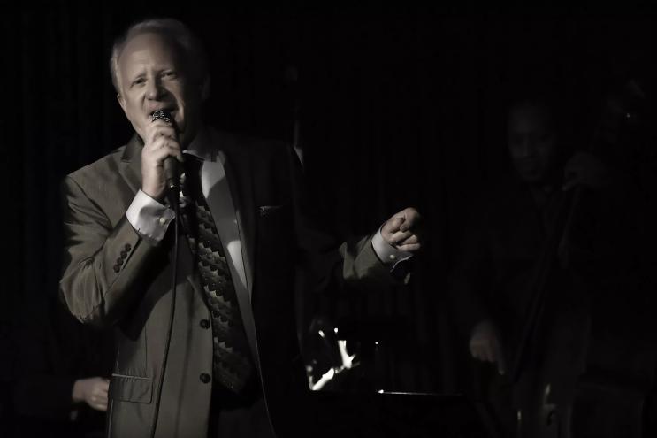 A man in a suit sings with a microphone on stage.