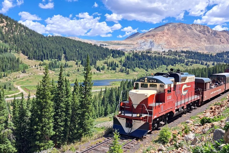 The Leadville Railroad train backdropped by evergreen trees and a rocky peak