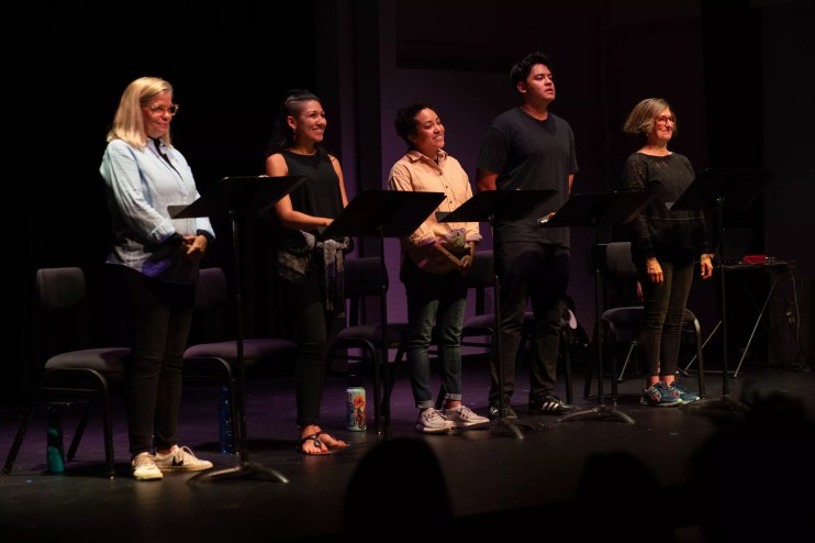 Actors stand by microphones on a stage