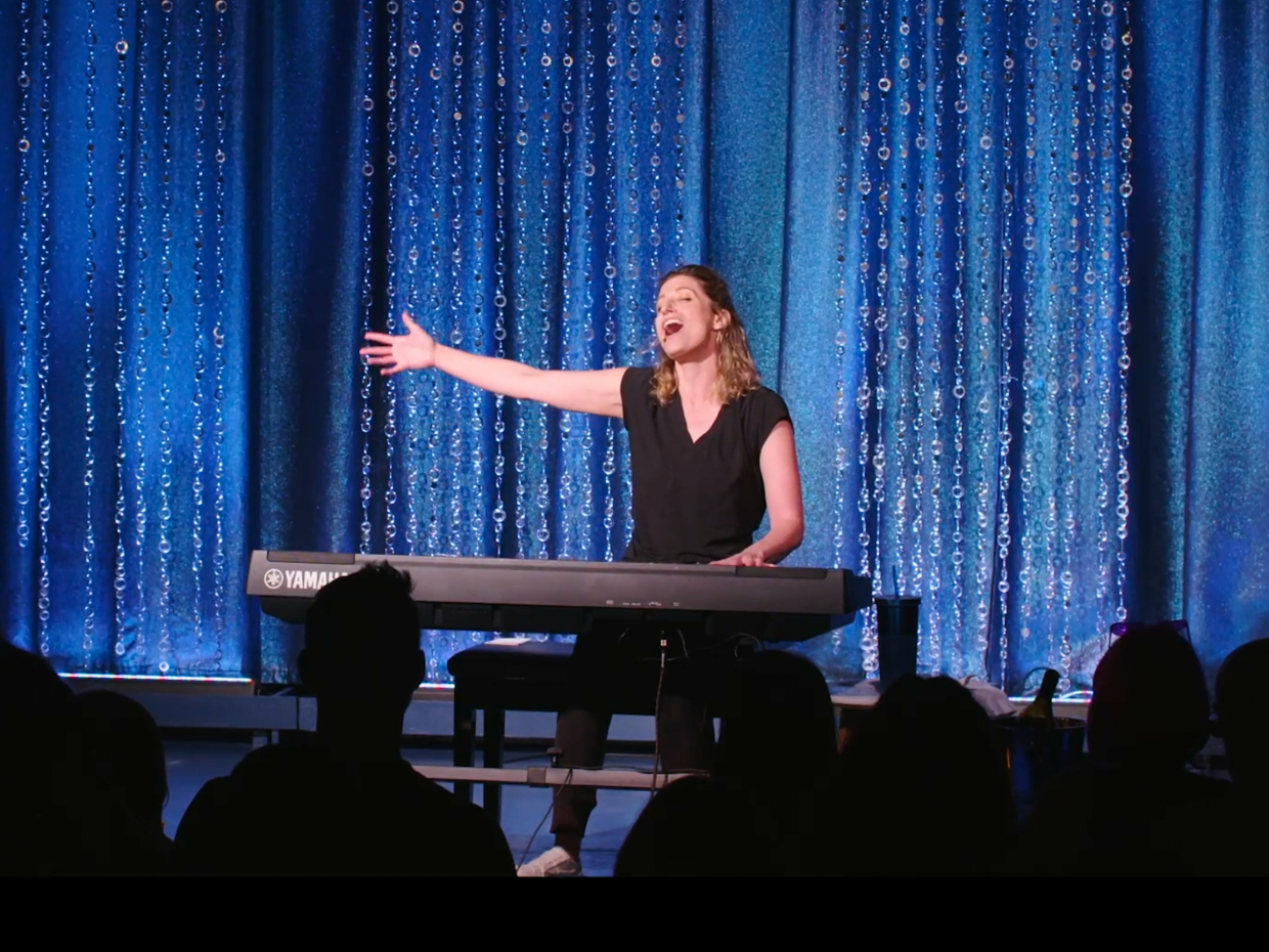 woman at piano in front of curtain.
