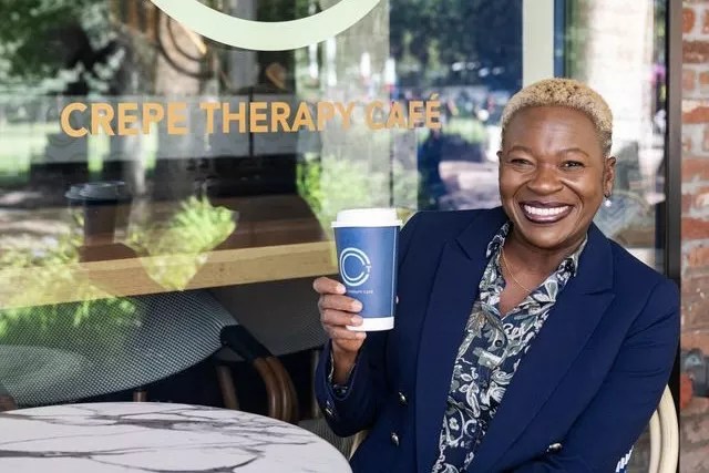 Chef Mawa McQueen seated outdoors and holding up a hot beverage cup from Crepe Therapy Cafe