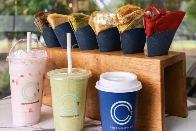 Various crepes and beverages from Crepe Therapy Cafe displayed on a white marble table