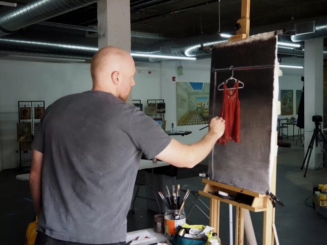 A man works on a painting of an orange dress
