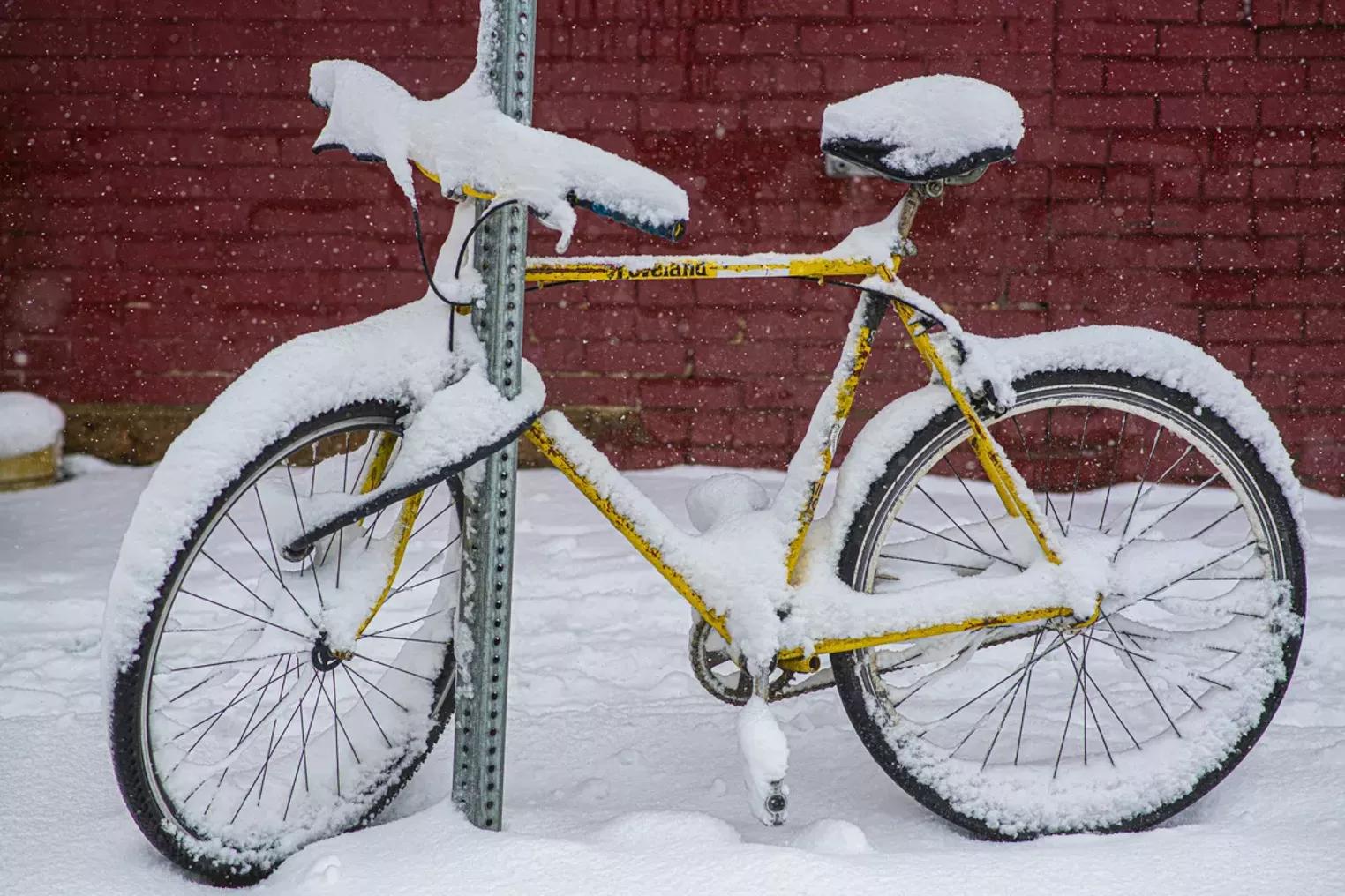 bike covered in snow , chained to signpost on the street