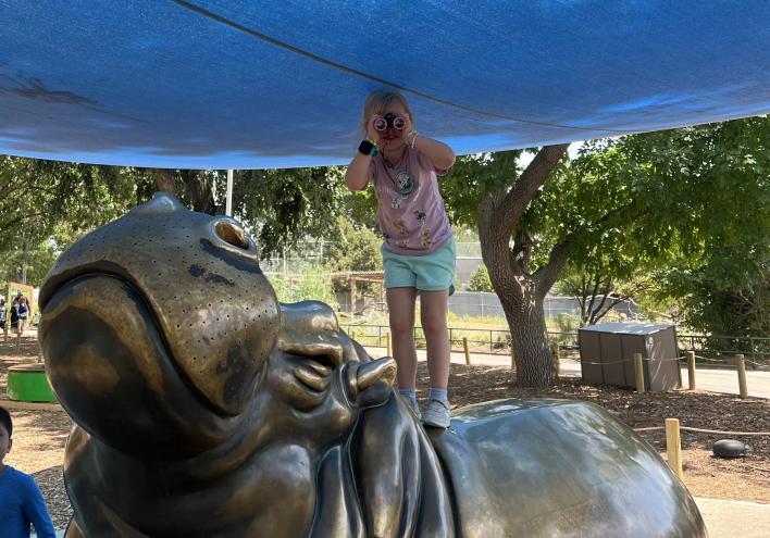 A girl with binoculars stands on a hippo statue