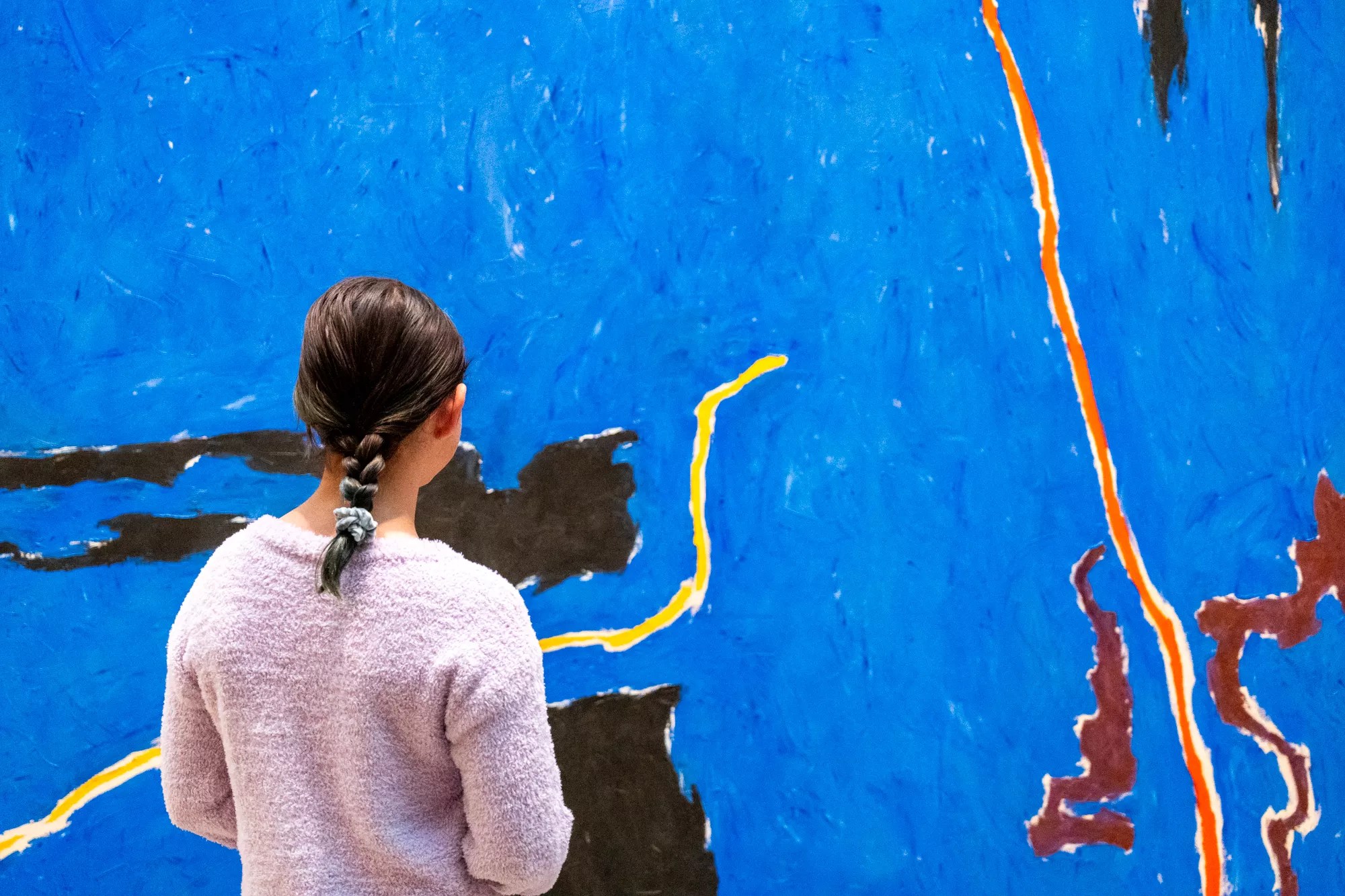 A girl looks at a large blue art piece
